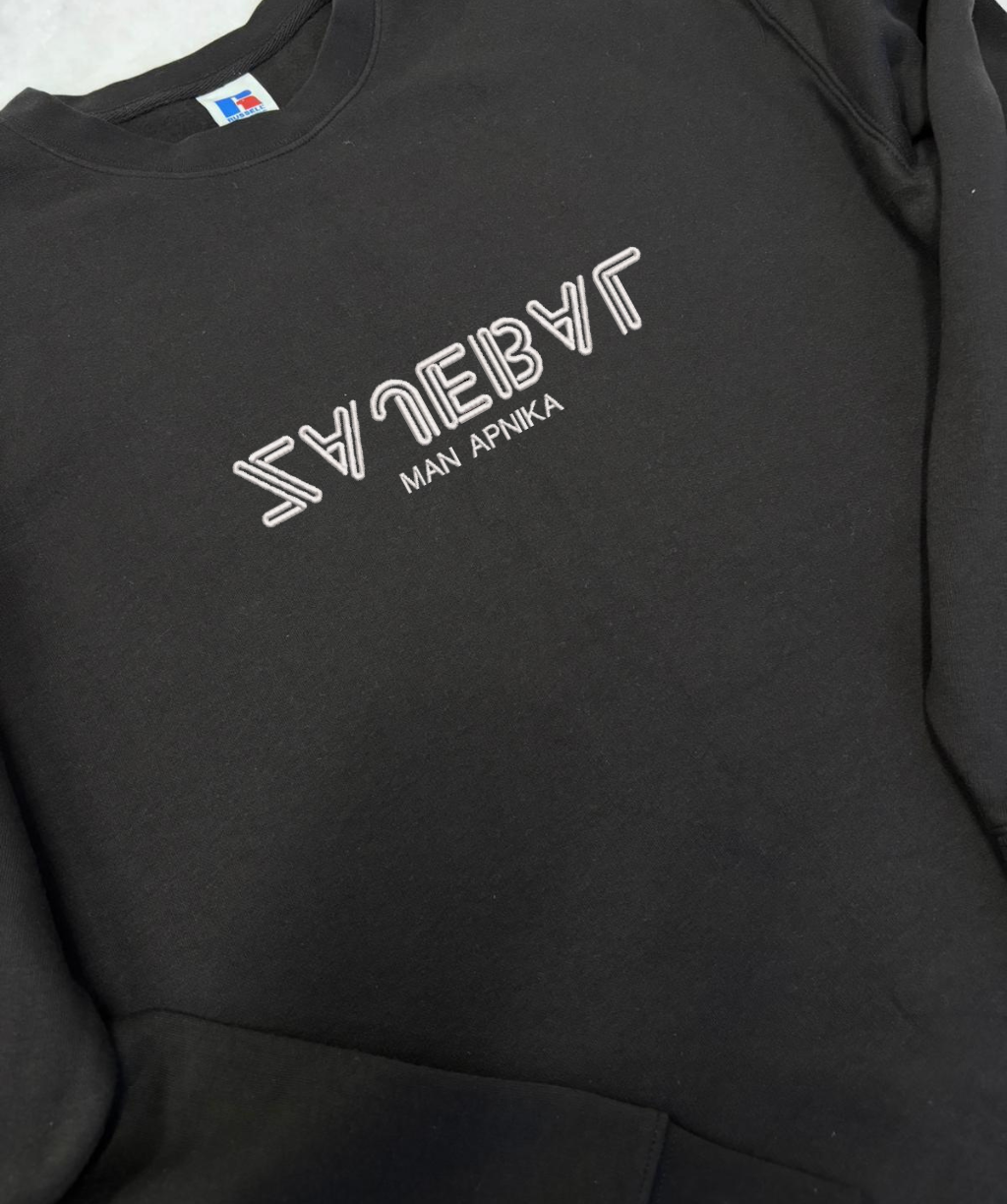 Izšūts teksts “… man apnika” uz melna unisex apģērba