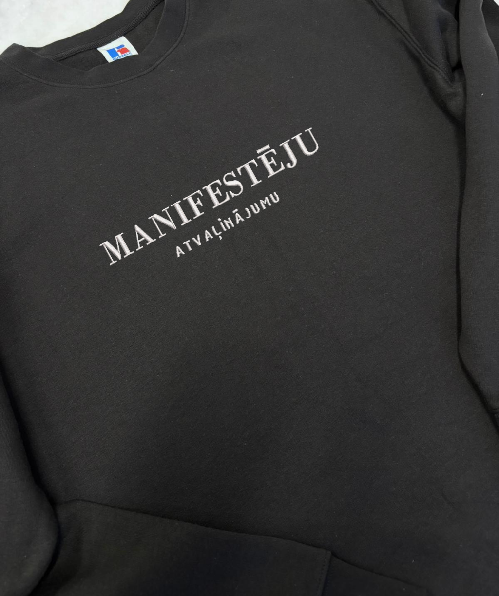 Unisex džemperis ar izšūtu tekstu “manifestēju”