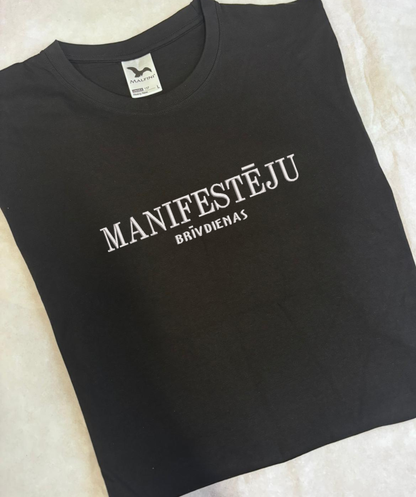 Izšūts teksts “Manifestēju” uz melna T-krekla