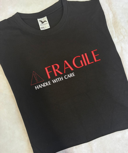 Izšūts teksts “Fragile, handle with care” uz melna unisex apģērba